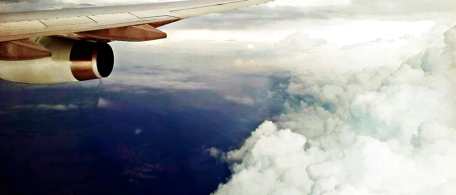 View from an airplane window, wing over clouds and coastline.